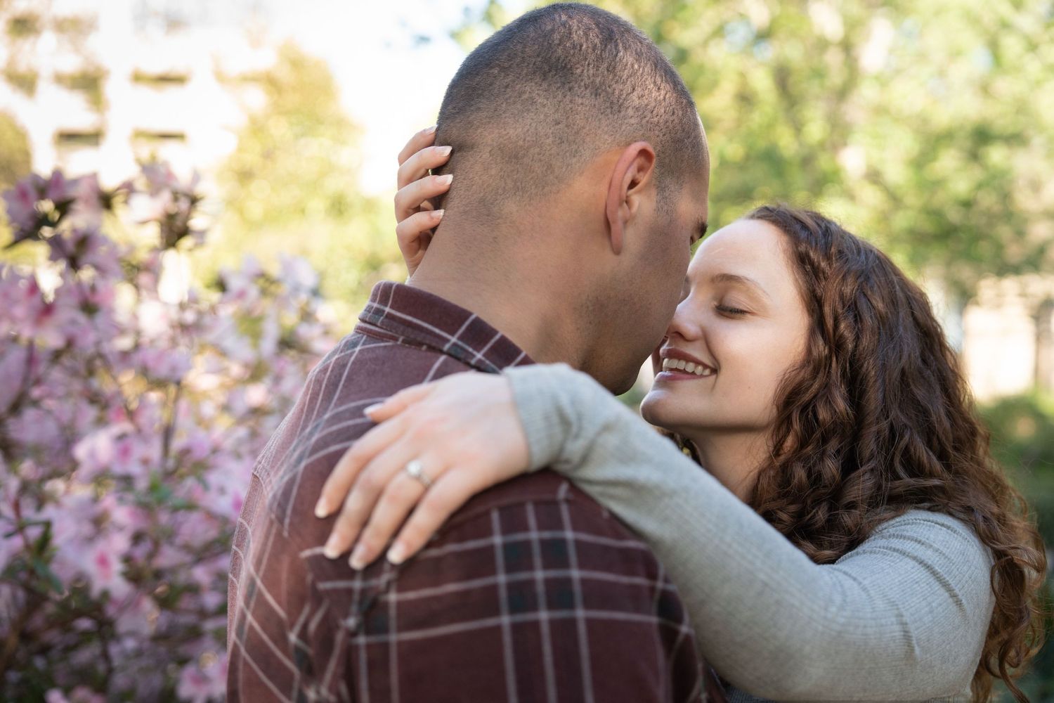 A couple shares a joyful embrace outdoors with cherry blossoms in the background.
