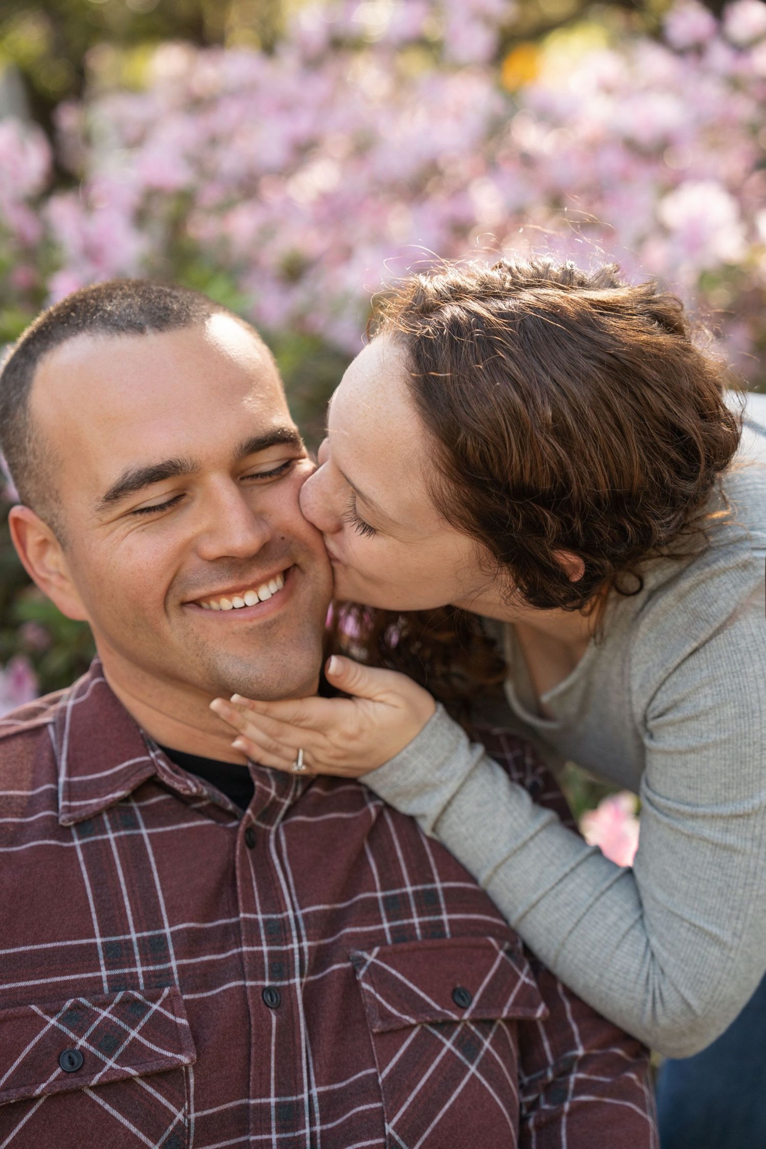 A sweet moment captured between two people with pink cherry blossoms blooming in the background.