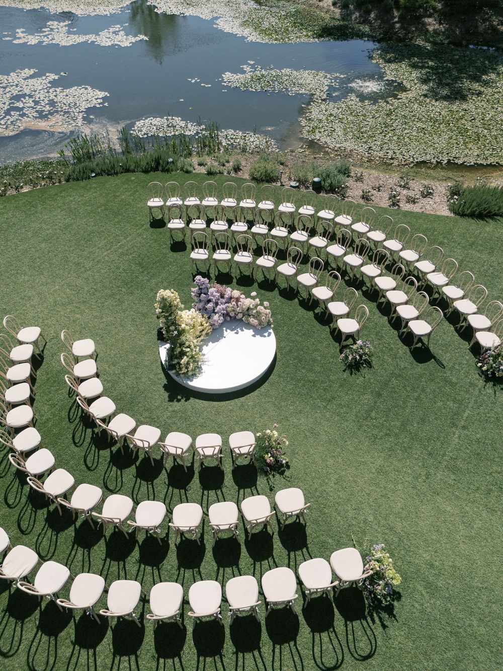 White chairs arranged in a curved spiral pattern on a green lawn for an outdoor wedding ceremony setup.