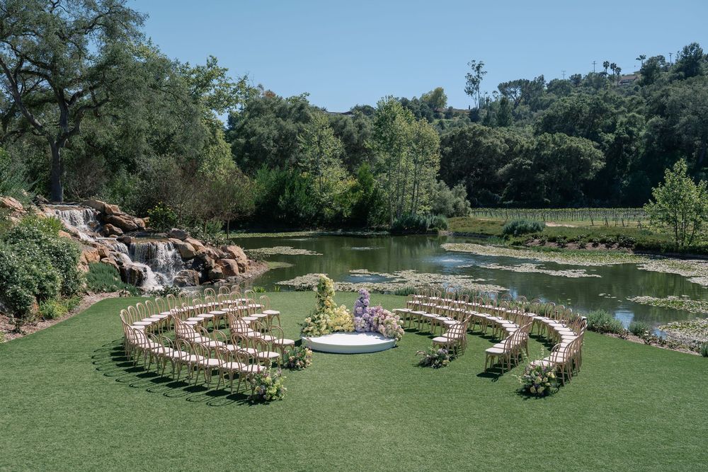 Outdoor wedding ceremony setup with curved rows of wooden chairs arranged in semicircles by a serene pond and waterfall.