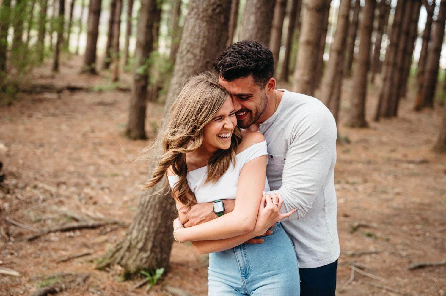 Romantic couple embraces while walking through a scenic forest path during an engagement photo session.