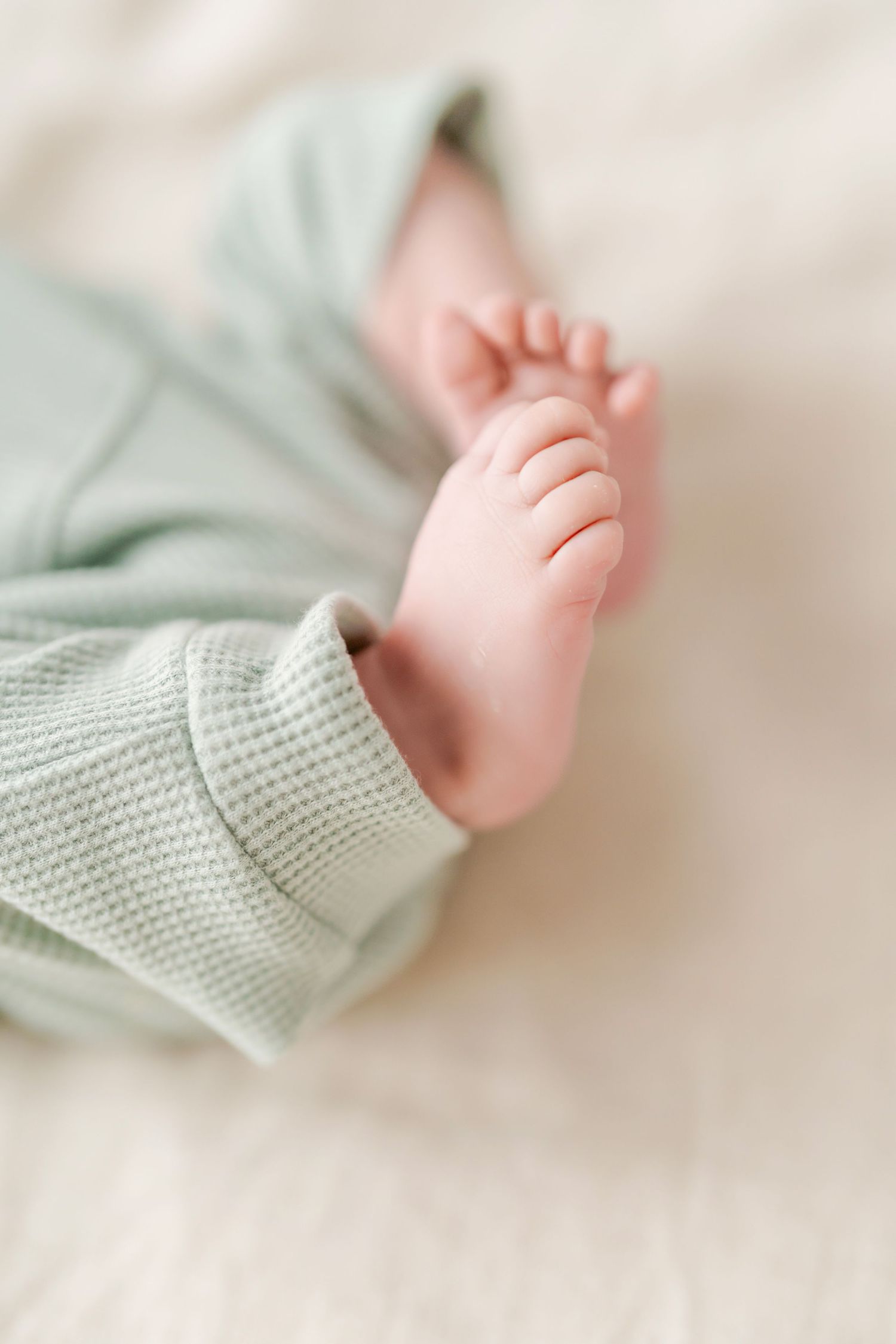 Close-up of tiny baby foot wearing soft mint green knit clothing against white background.