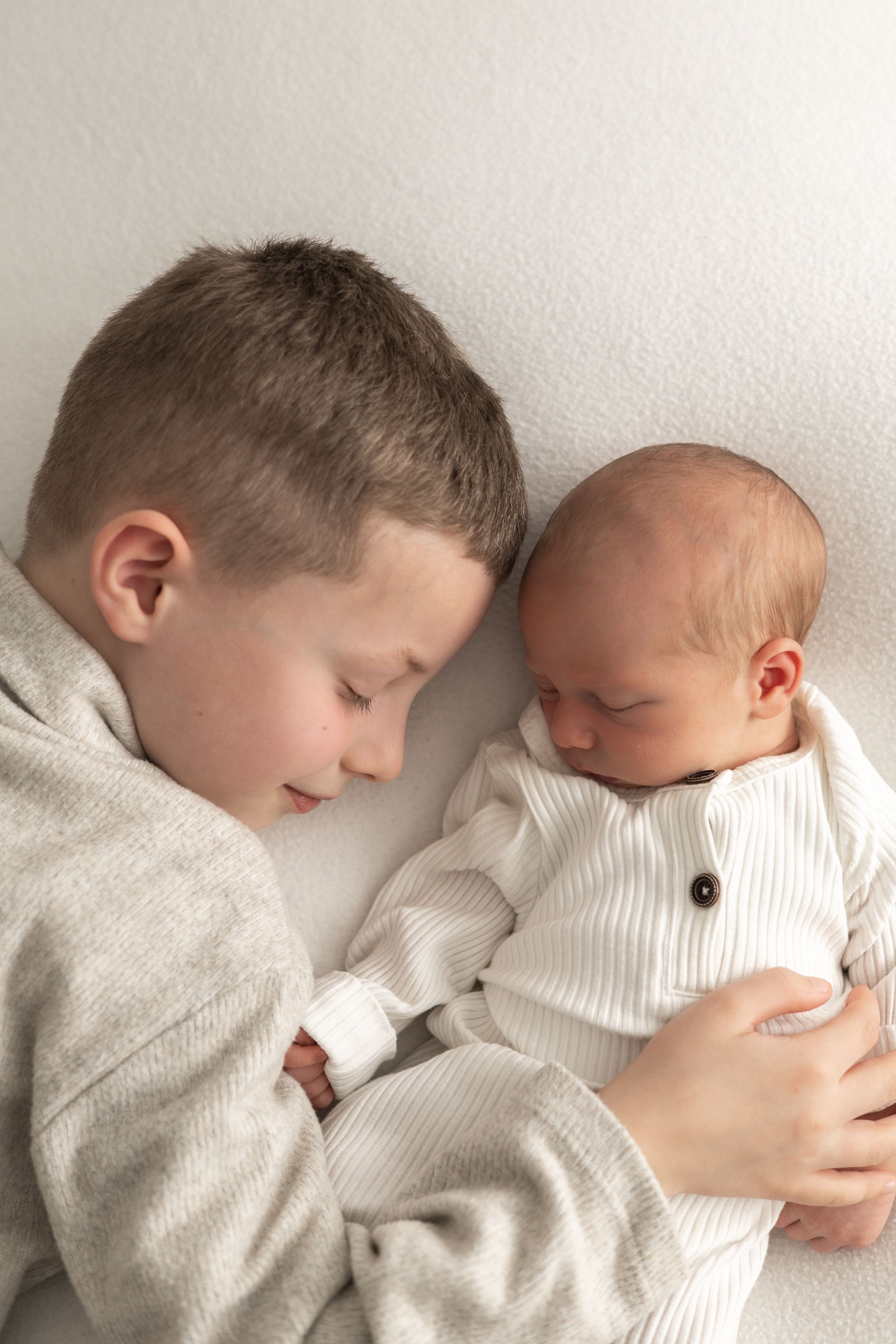 Young boy tenderly holds sleeping newborn baby sibling natural newborn photography Nottingham