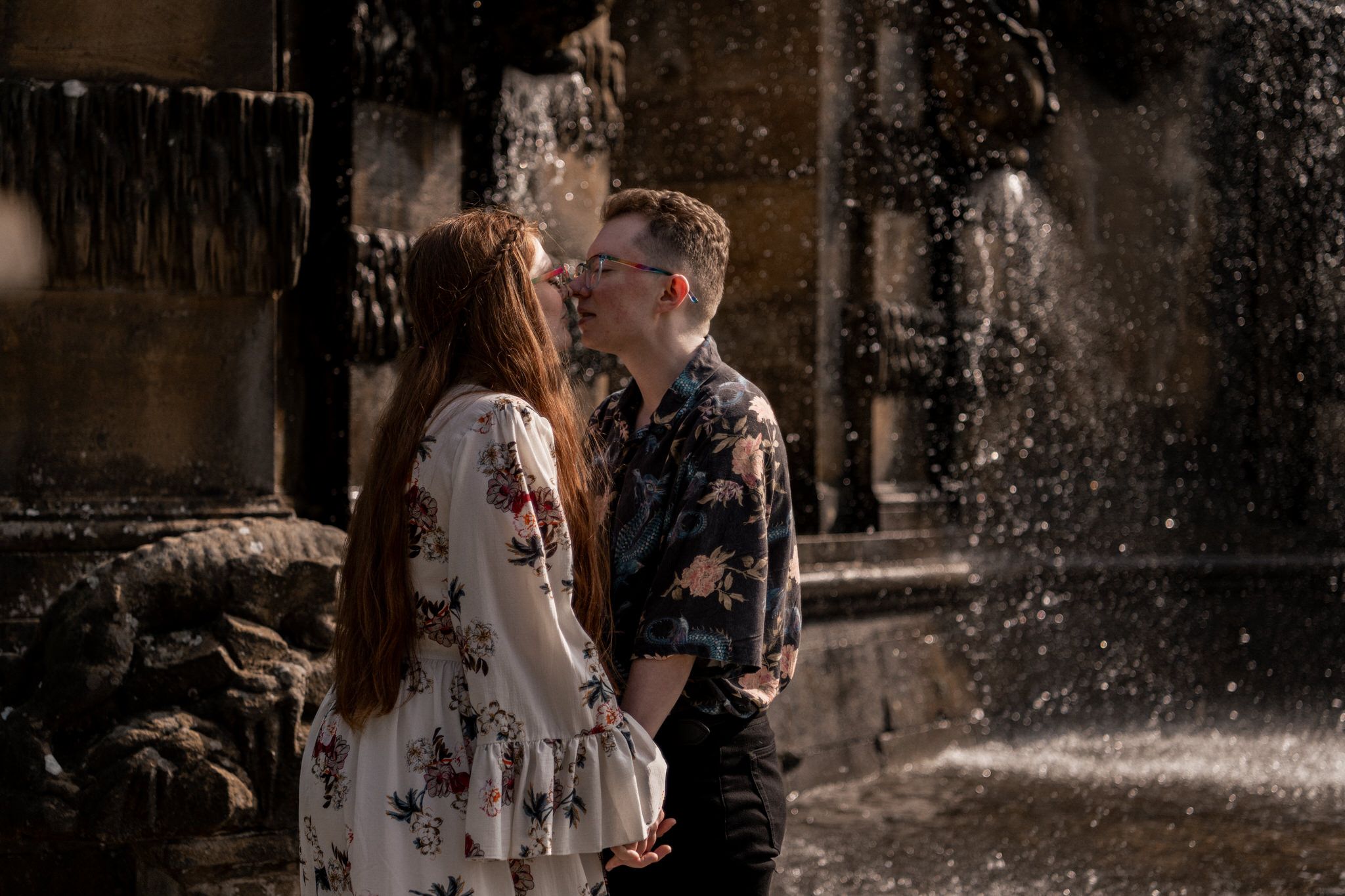 A romantic couple embraces in the rain against a historic stone building backdrop.