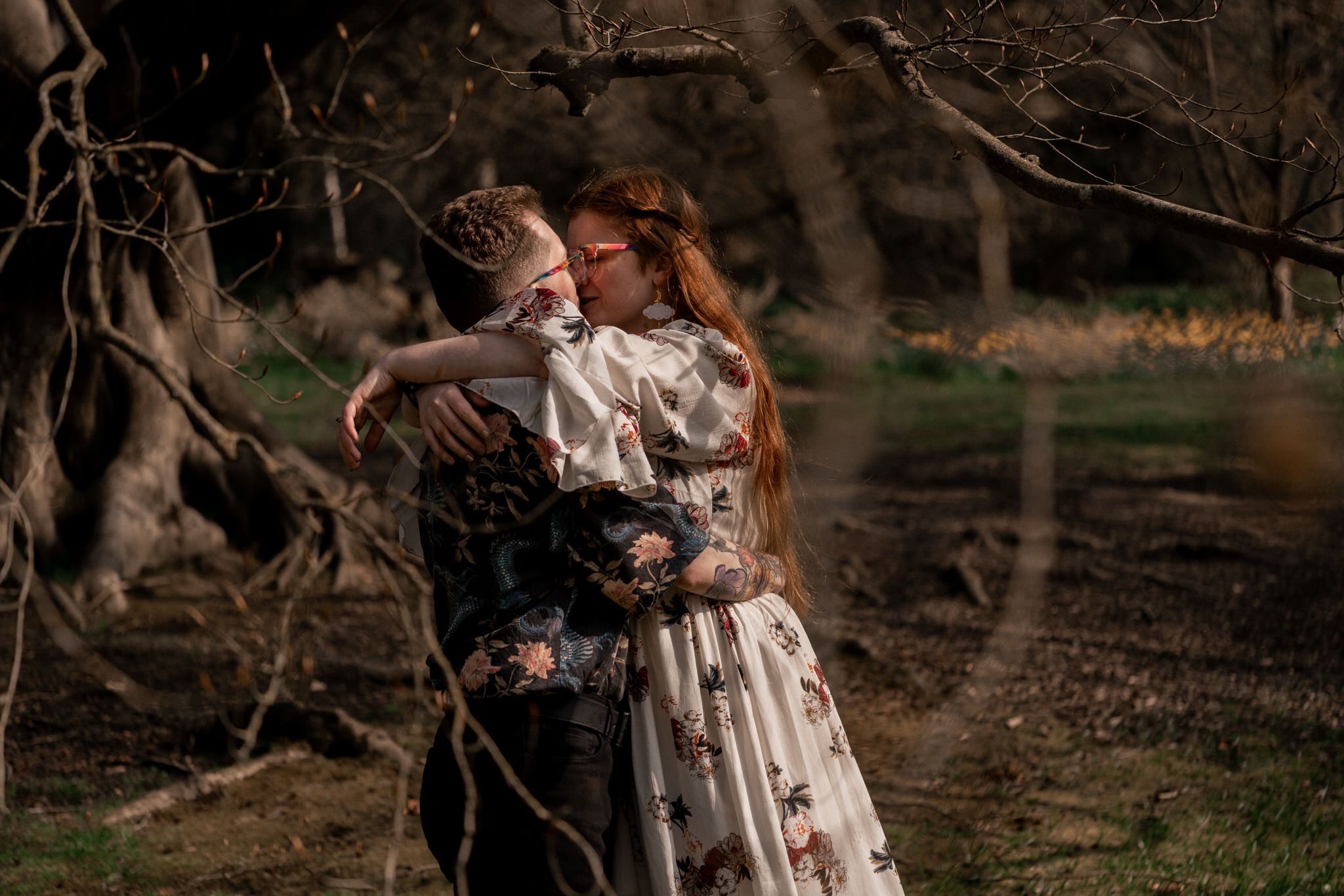 A couple in vintage-style clothing embraces in a romantic forest setting at sunset.