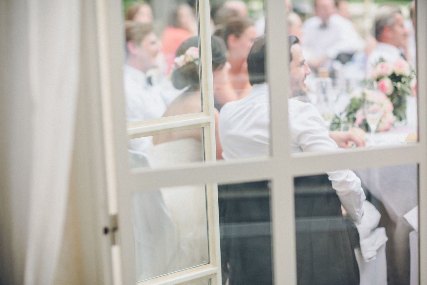 Wedding reception at a French château captured through a window with soft light, creating an intimate and cinematic destination wedding atmo