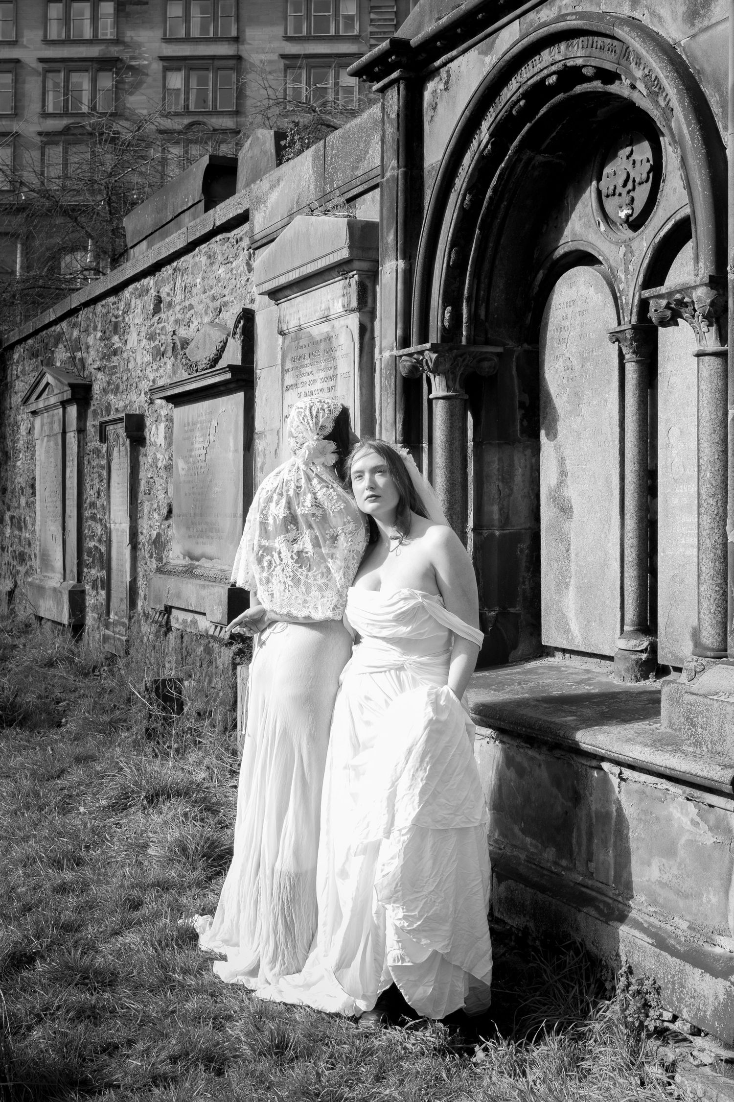 A figure in a flowing white dress poses against stone architecture in a moody black and white photo series.