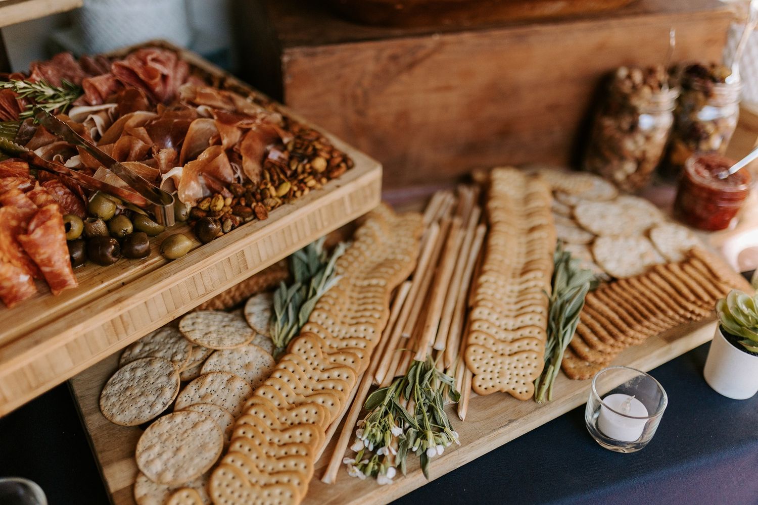 Elegant charcuterie board with crackers, cured meats, olives, and herbs on wooden boards at a catered event.