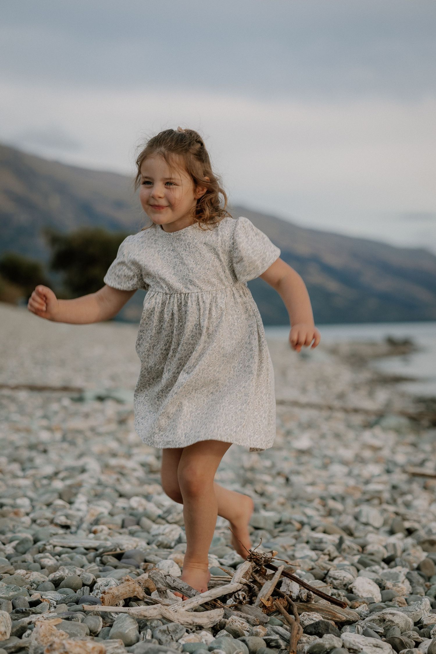Young girl in floral dress playing at Lake Wakatipu, Homestead Bay in Queenstown during a family photoshoot.