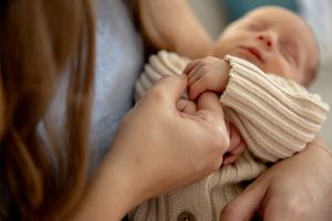 Mum holding new born's hand  in lounge room at new born professional photo shoot