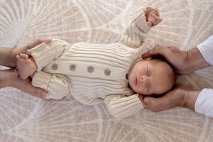 Father cradling baby's head and mother holding feet in lounge room at new born professional photo shoot