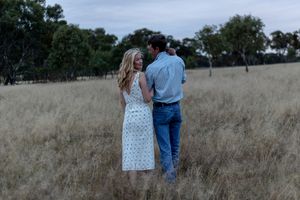 Father holding new born and mother holding onto father while walking through a paddock during a professional newborn photo shoot.