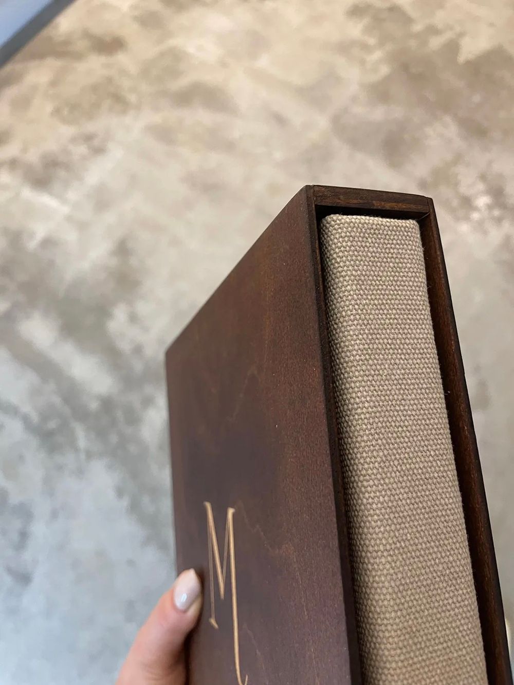 Detailopname van een donkerhouten doos met een beige fotoalbum van canvas met gouden initialen.