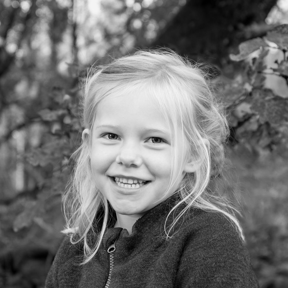 Black and white portrait of a smiling blonde little girl outdoors among trees.