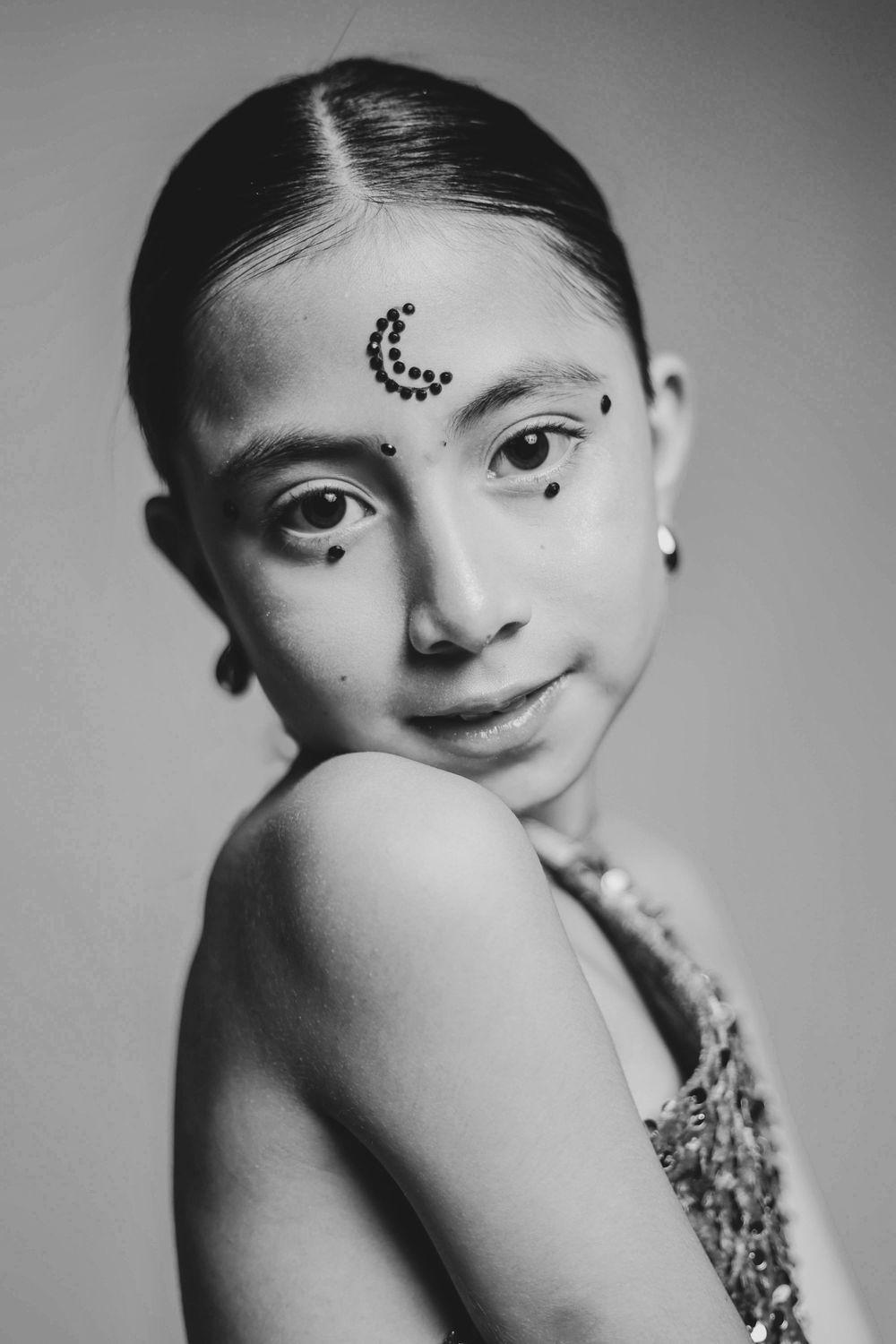 Black and white portrait of a young woman with crescent moon rhinestone forehead art and subtle dot accents.
