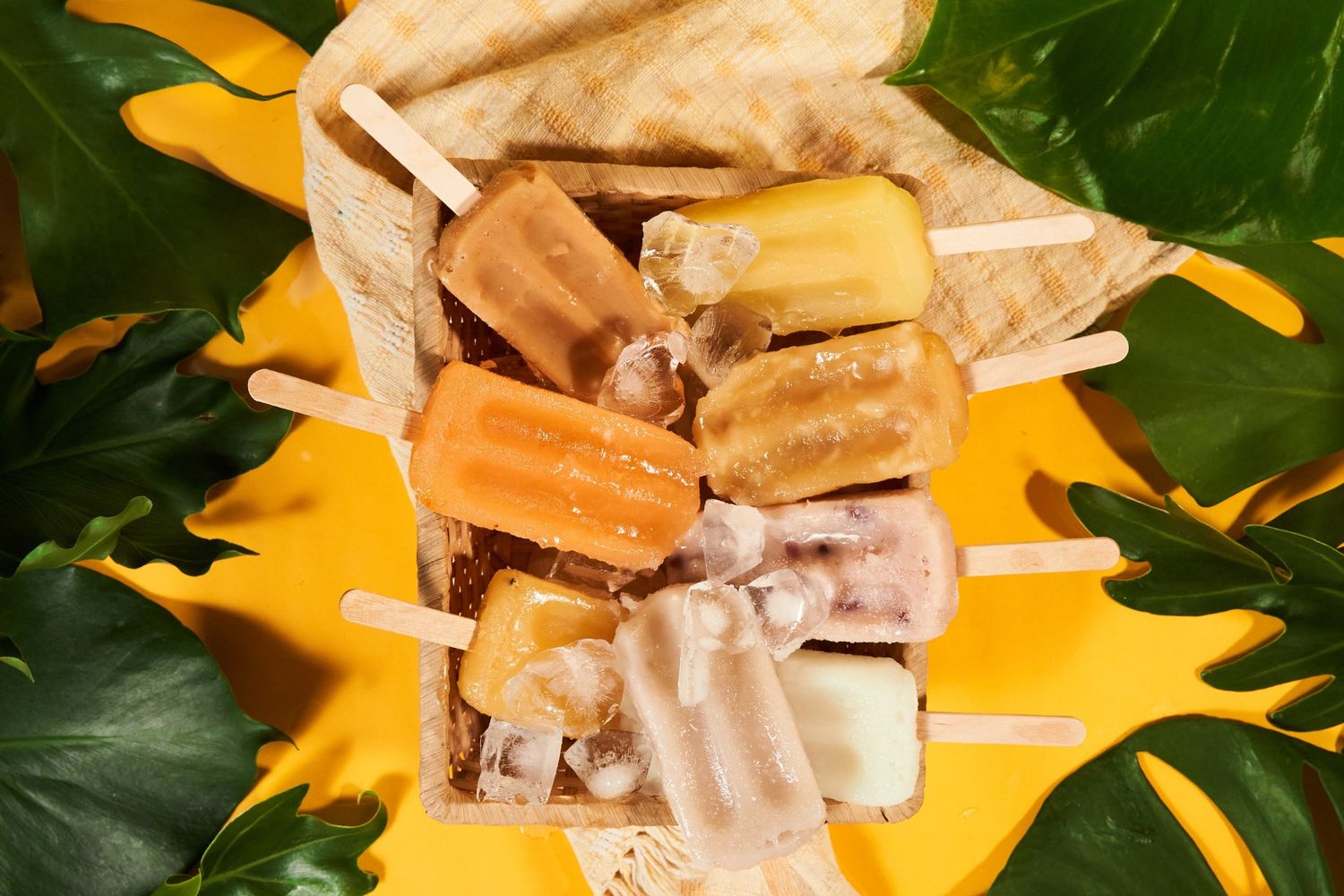 Colorful homemade popsicles arranged around a pinecone on a rustic table with newspaper background.