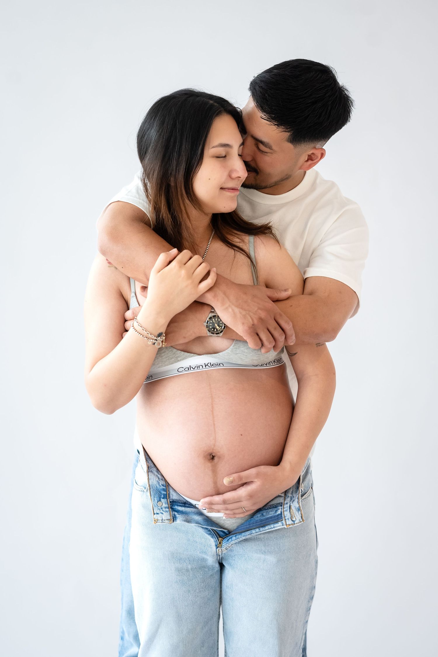 Intimate maternity photo of a couple embracing against white background as they celebrate their pregnancy.