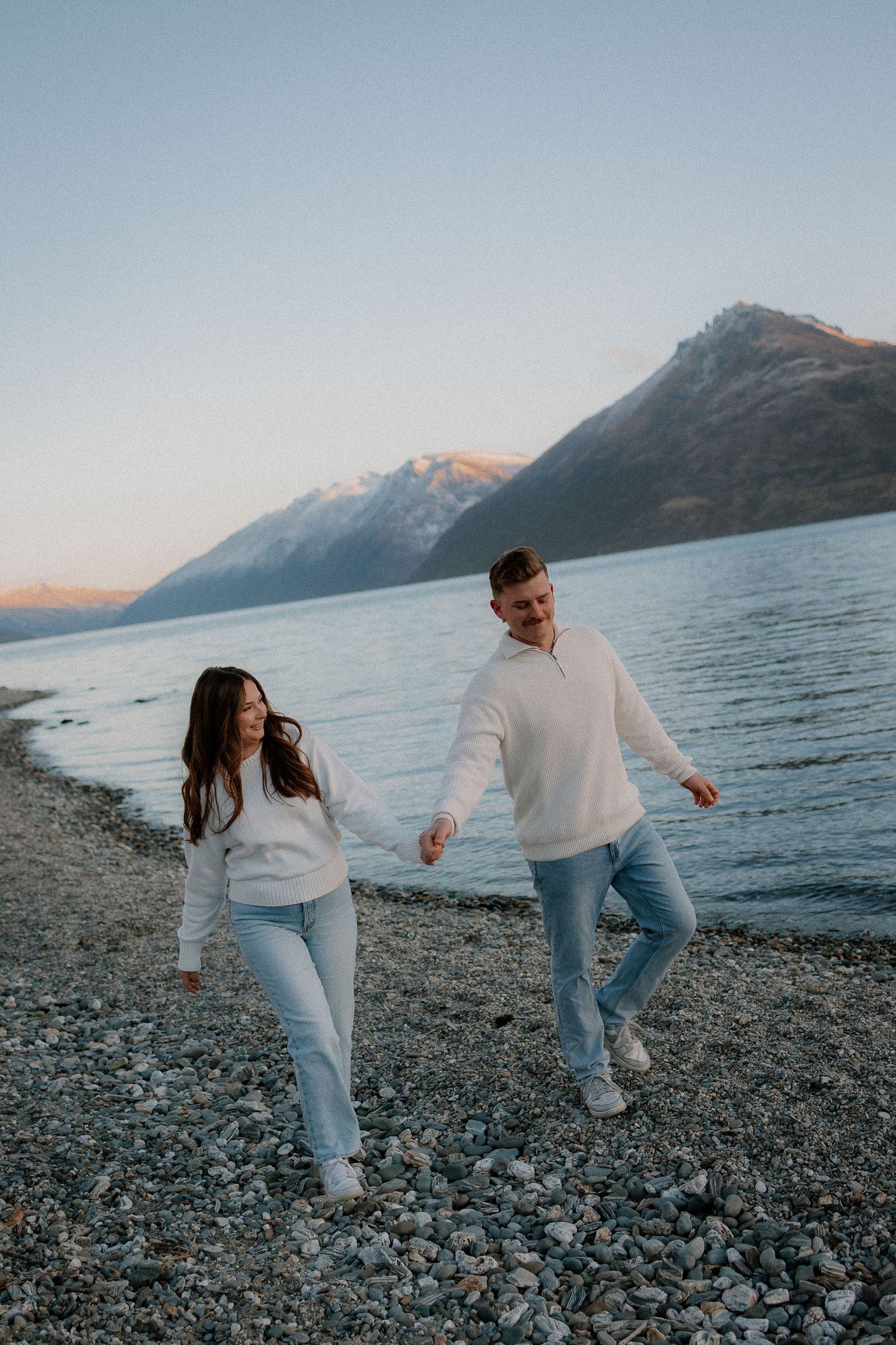 A couple dances together on a scenic beach at sunset with mountains in the background.