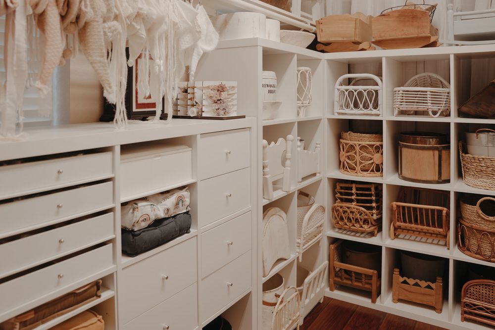 Organized white walk-in closet with shelving units, wicker baskets, and drawers for stylish home storage solutions. Paloma Schell