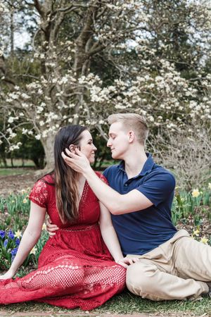 Romantic couple lying in spring garden with blooming cherry blossoms and daffodils, woman in red lace dress.