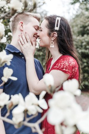 Intimate couple sharing tender moments among white spring blossoms, she in red lace and he in navy blue.