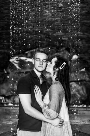 A romantic black and white photo of a couple embracing under falling water droplets.