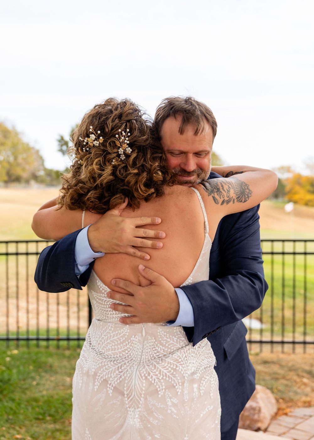 Emotional groom in navy suit hugging bride in lace wedding dress during first look outdoors  at a Venue on the Ridge in Elkhorn, NE