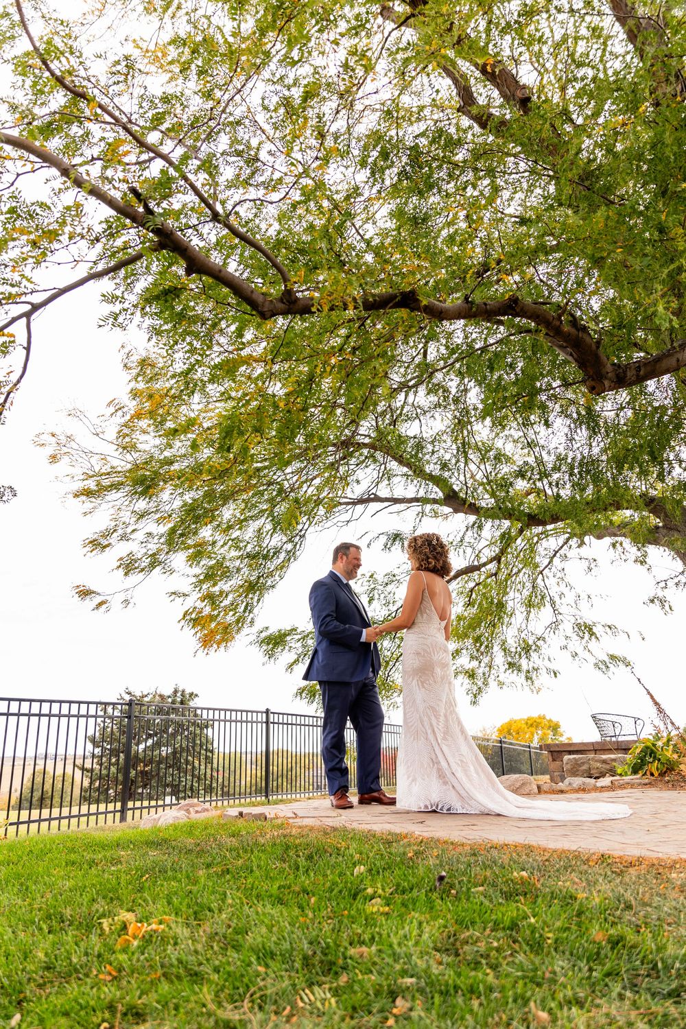 Bride and groom holding hands under a large green tree at outdoor wedding venue,  at a Venue on the Ridge in Elkhorn, NE