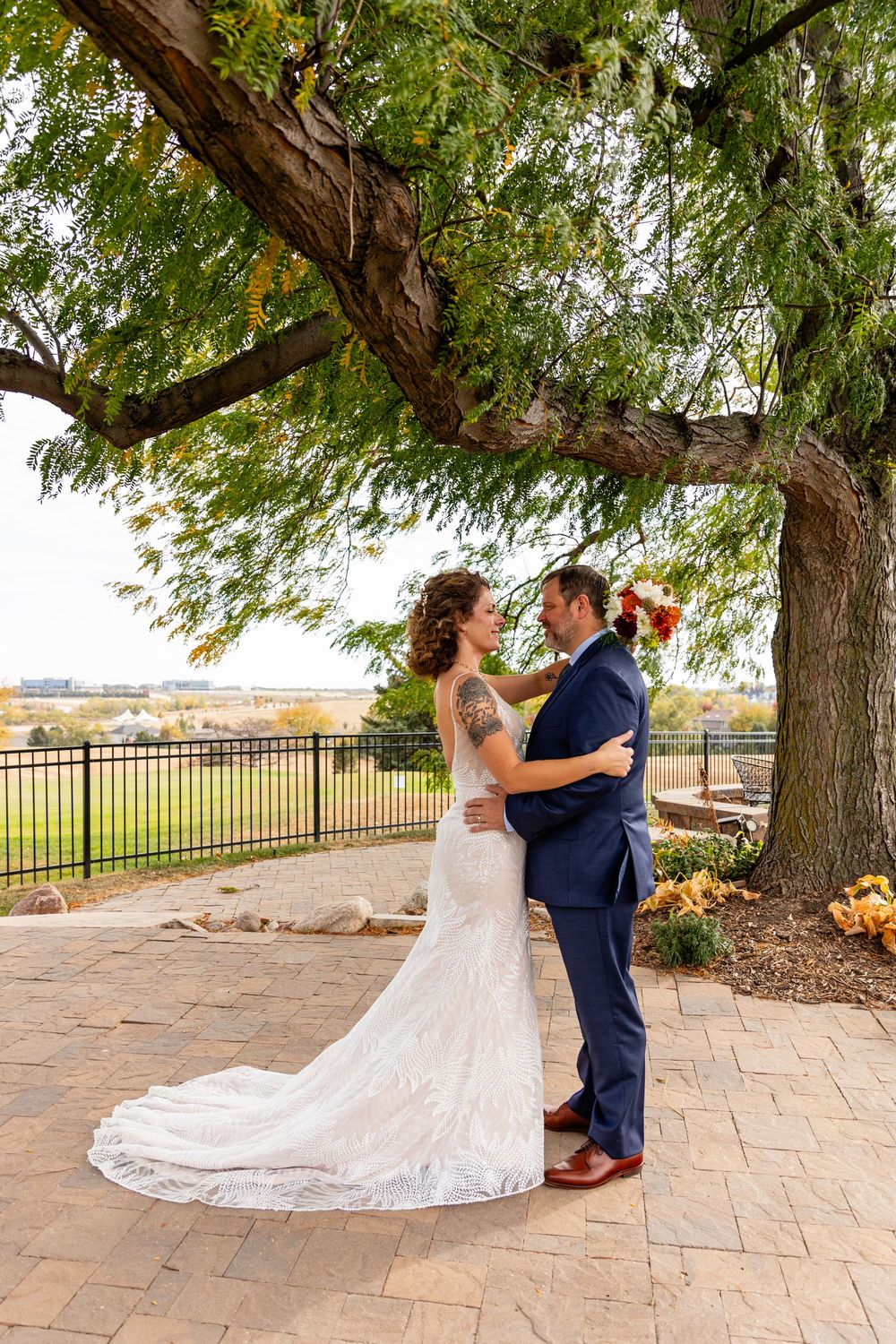 Bride and groom share a romantic first look under a large tree on a patio  at a Venue on the Ridge in Elkhorn, NE