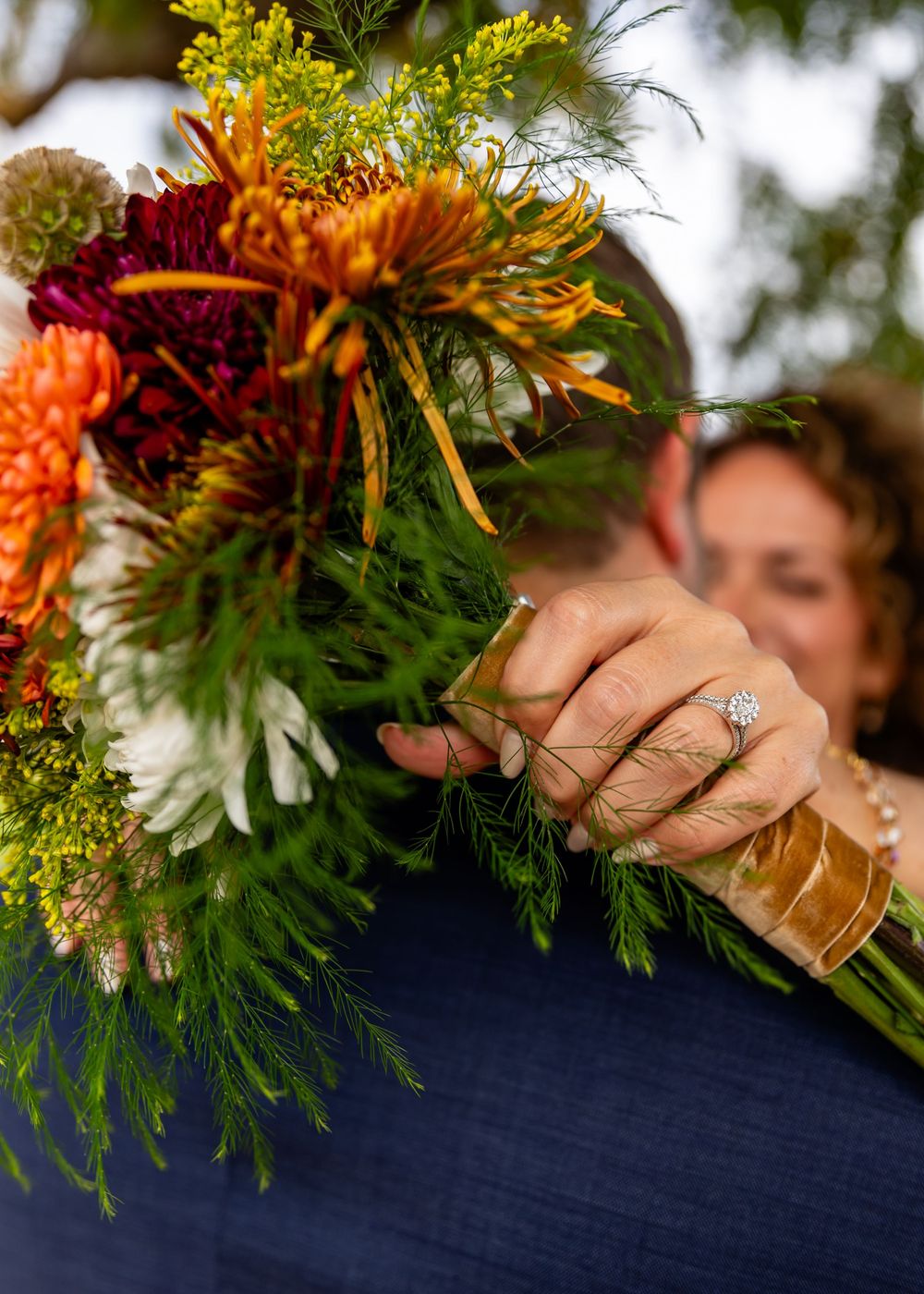Bride holds vibrant autumn wedding bouquet with orange, red, and yellow blooms.
