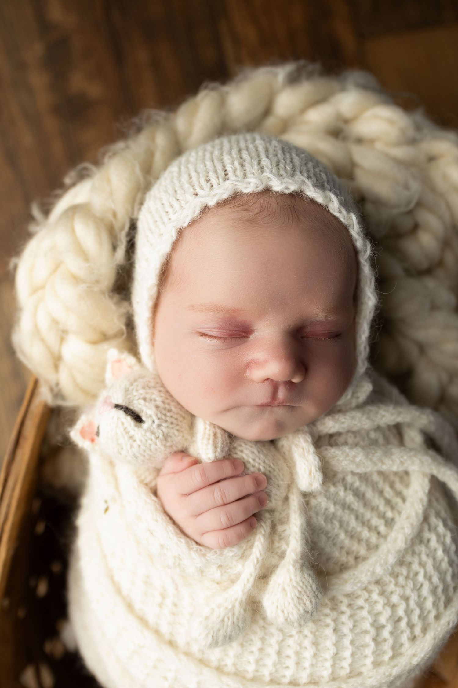 Sleeping newborn baby wrapped in cream knit swaddle and bonnet, resting peacefully in a cozy basket.