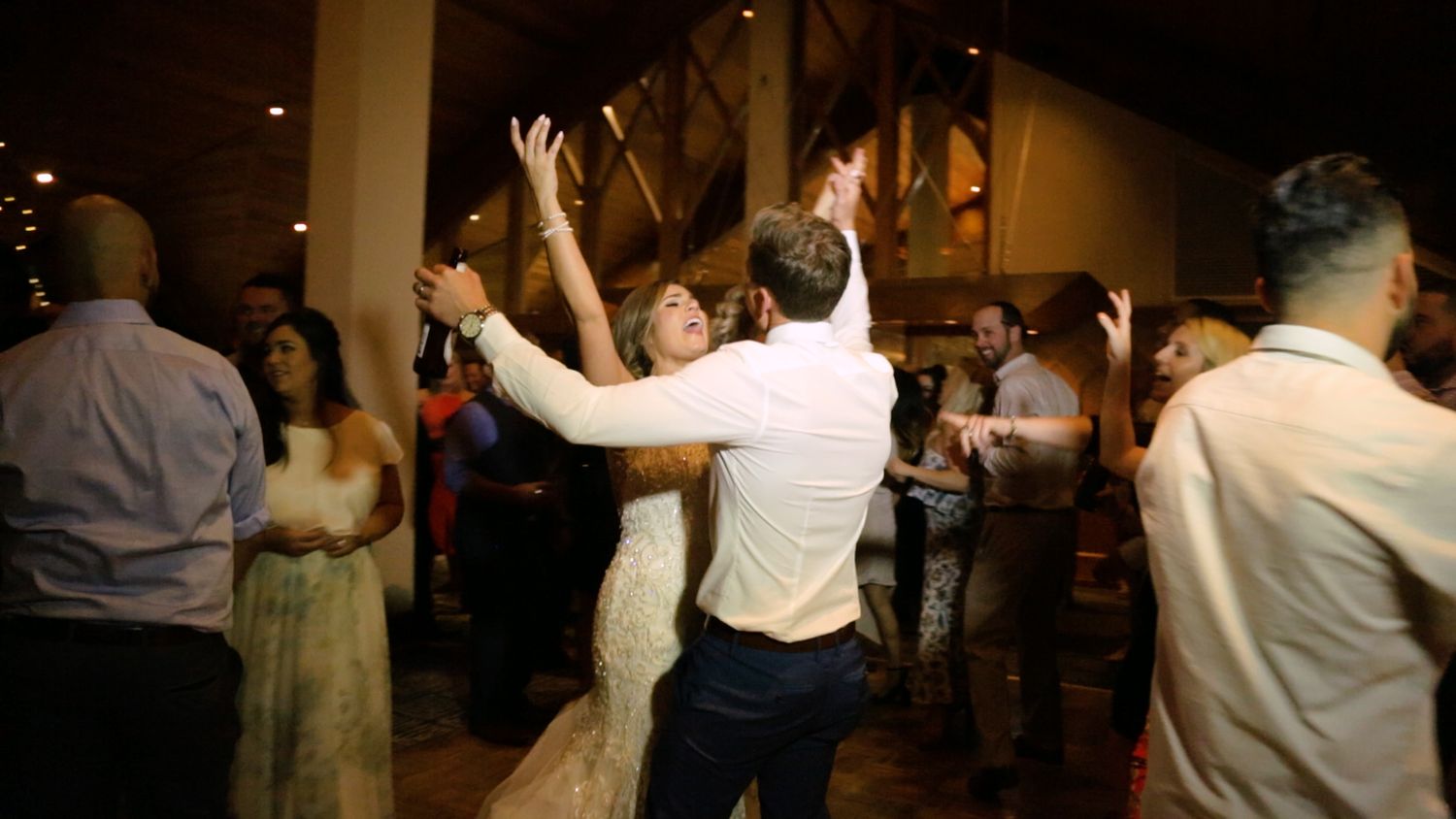 Bride and groom dancing joyfully at wedding reception surrounded by guests in elegant venue.