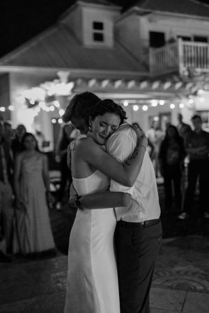 A tender embrace on the dance floor at an evening wedding reception with string lights glowing in the background.
