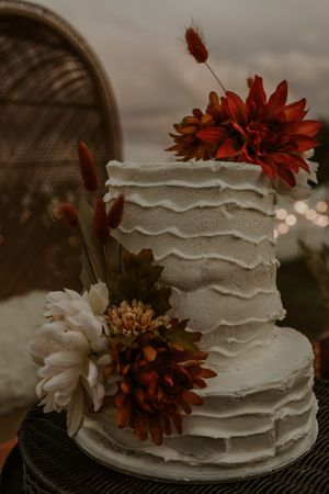 A rustic white wedding cake decorated with orange and white dahlias photographed in a moody, romantic style.