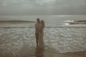 A couple stands together in the ocean waves at sunset creating a romantic silhouette against the horizon.