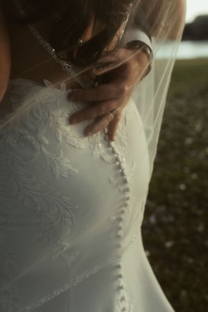 Close-up detail of an elegant white wedding dress with delicate lace embroidery and button closures along the back.