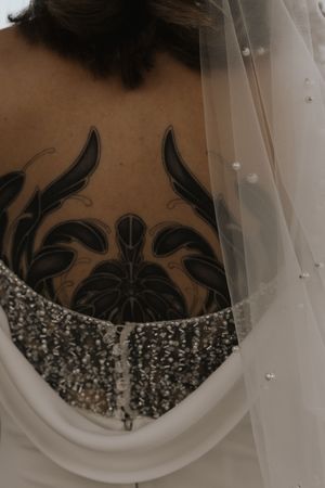 A close-up view of an ornate black tattoo design peeking above a sparkly beaded wedding dress neckline.
