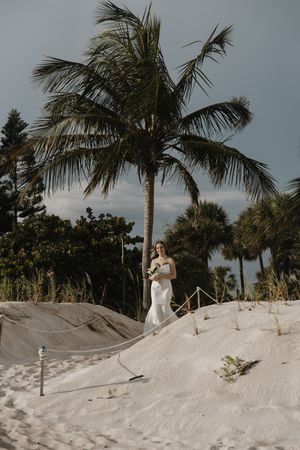 A wedding couple walks along a pristine white sand beach with palm trees swaying in the tropical breeze.
