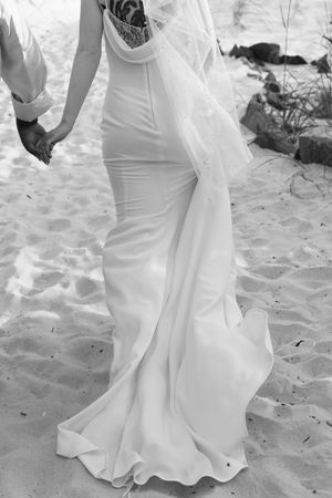 A series of wedding dress photos showing the flowing white gown's train and hem details against sandy beach background.