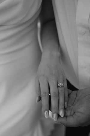 Close-up black and white photo of hands wearing wedding rings against white fabric.