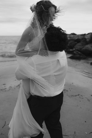 A romantic black and white beach photoshoot featuring an ethereal flowing white dress caught in the coastal breeze.
