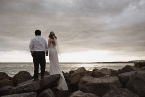 A couple stands together on rocky coastal cliffs at sunset overlooking a dramatic stormy ocean view.