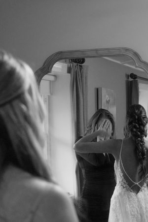 Black and white photo series showing a bride getting ready in a room with mirrors and natural lighting.