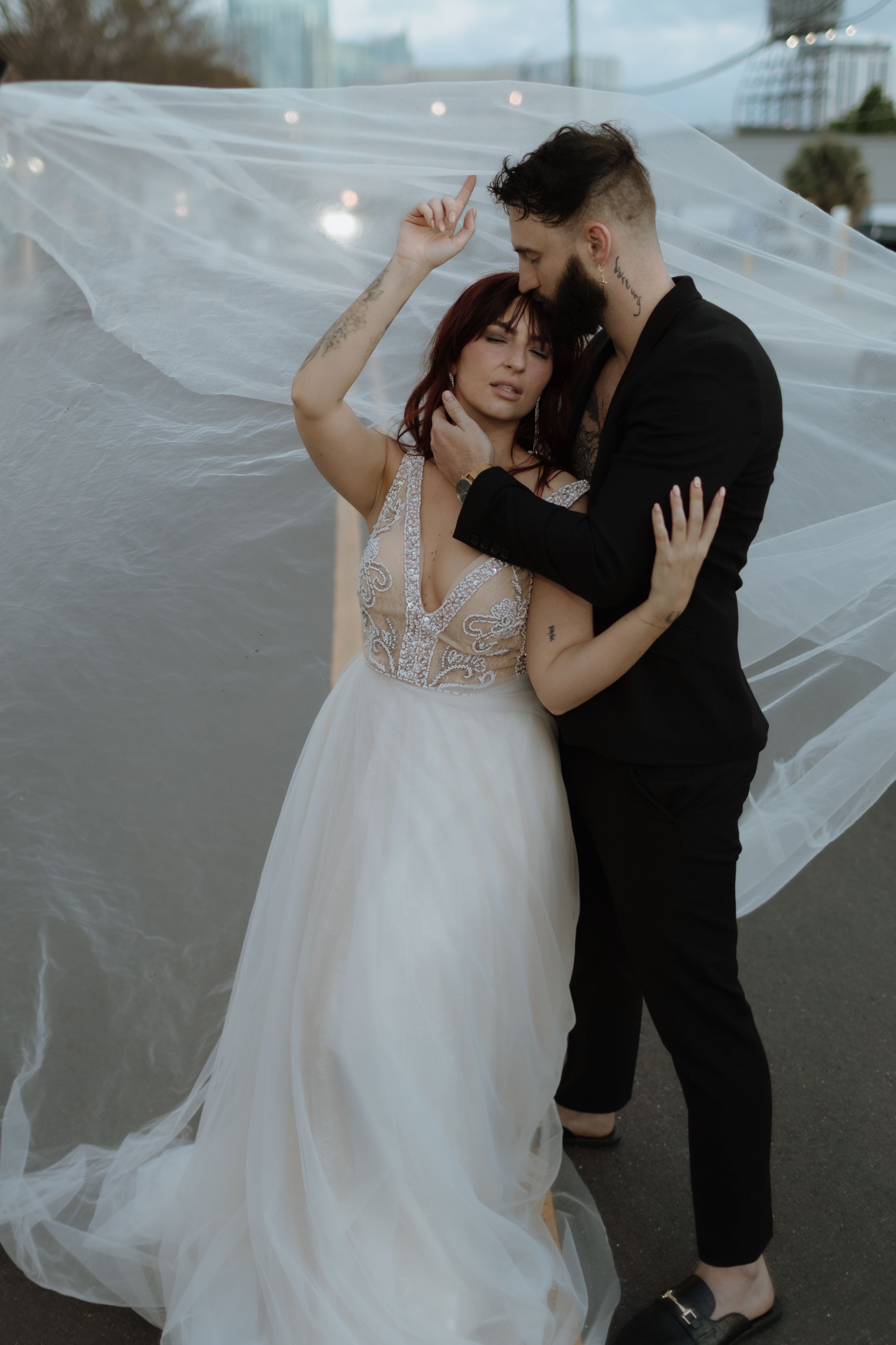 A couple in wedding attire dances romantically as a flowing white veil billows in the breeze.