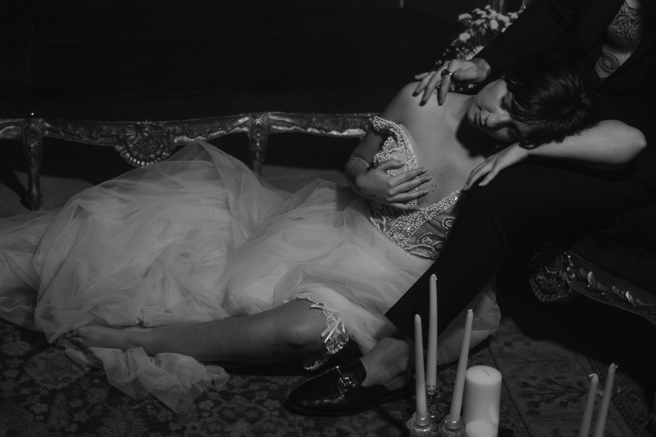 A vintage black and white photograph shows a person reclining on a couch in an elegant interior setting.
