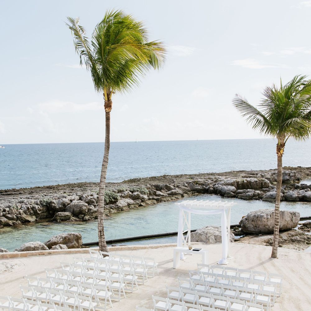 Palm trees sway in the breeze along a tropical beachfront wedding setup with white chairs facing the ocean.