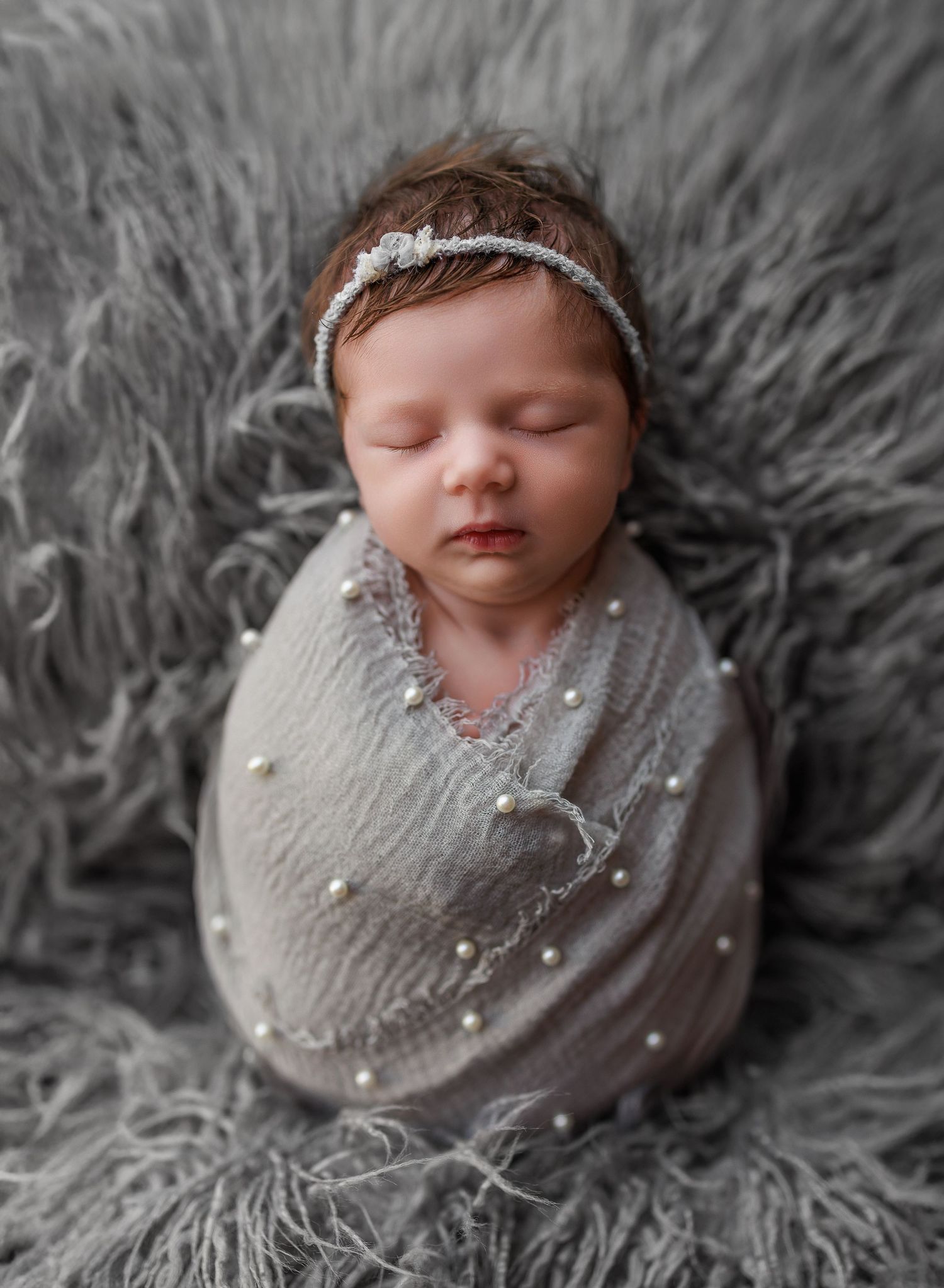 Photo of a newborn baby girl swaddled in a gray swaddle with pearls