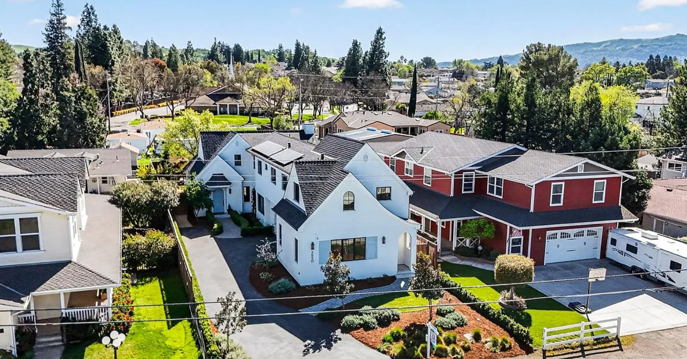 Aerial view of residential neighborhood with single-family homes and green yards surrounded by tall evergreen trees.