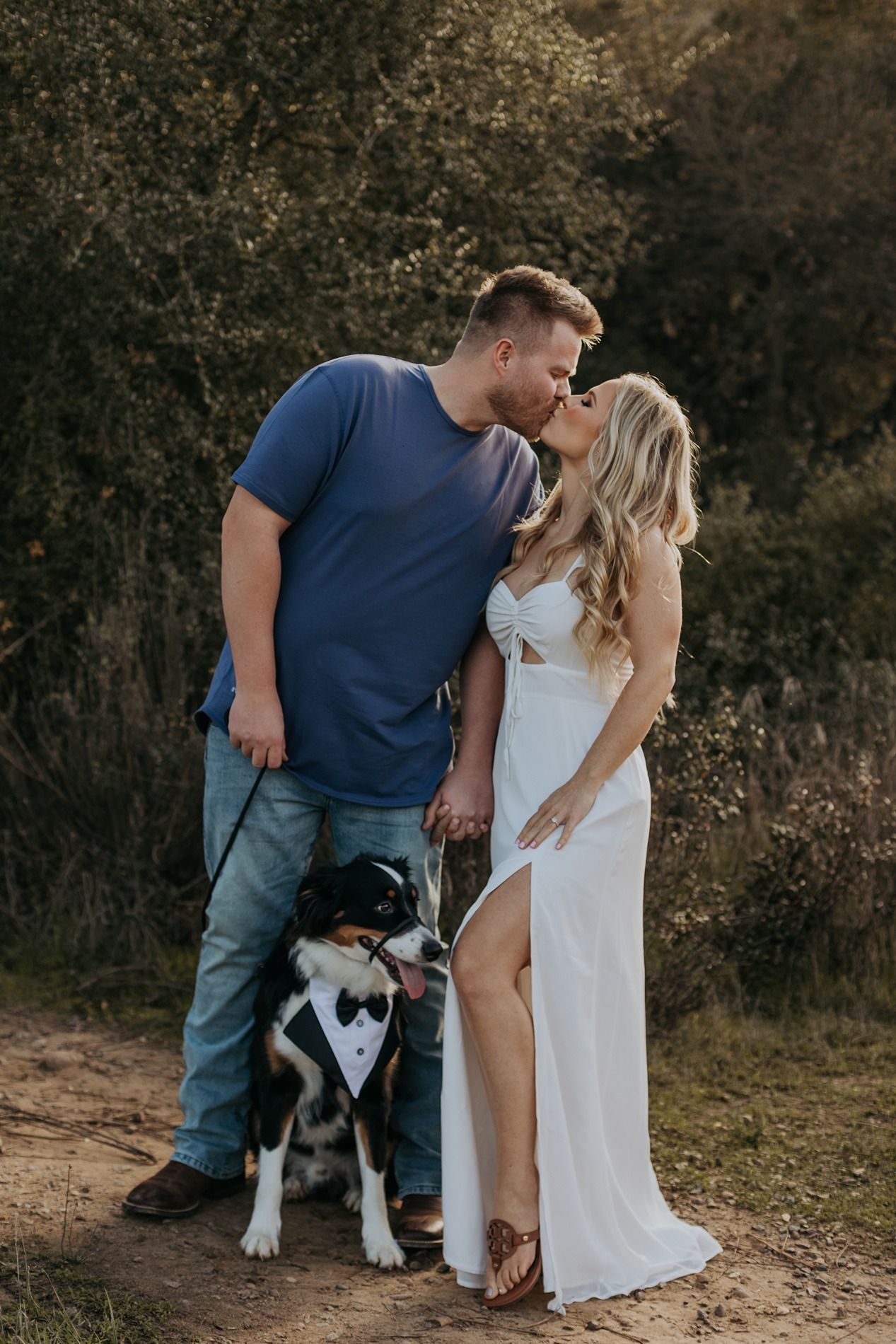 A couple in formal attire shares tender moments with their dog during an outdoor photoshoot at sunset in San Diego.
