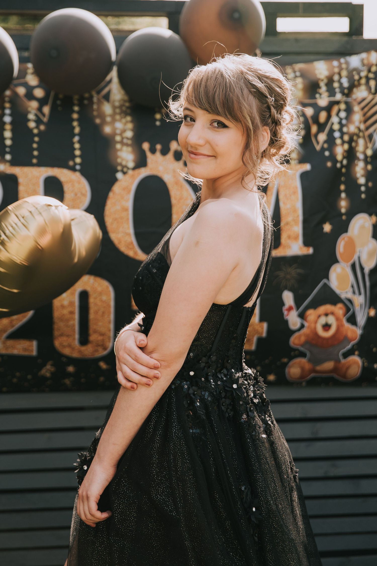 Woman in elegant black tulle dress poses at festive party with 2020 decorations and string lights in background.